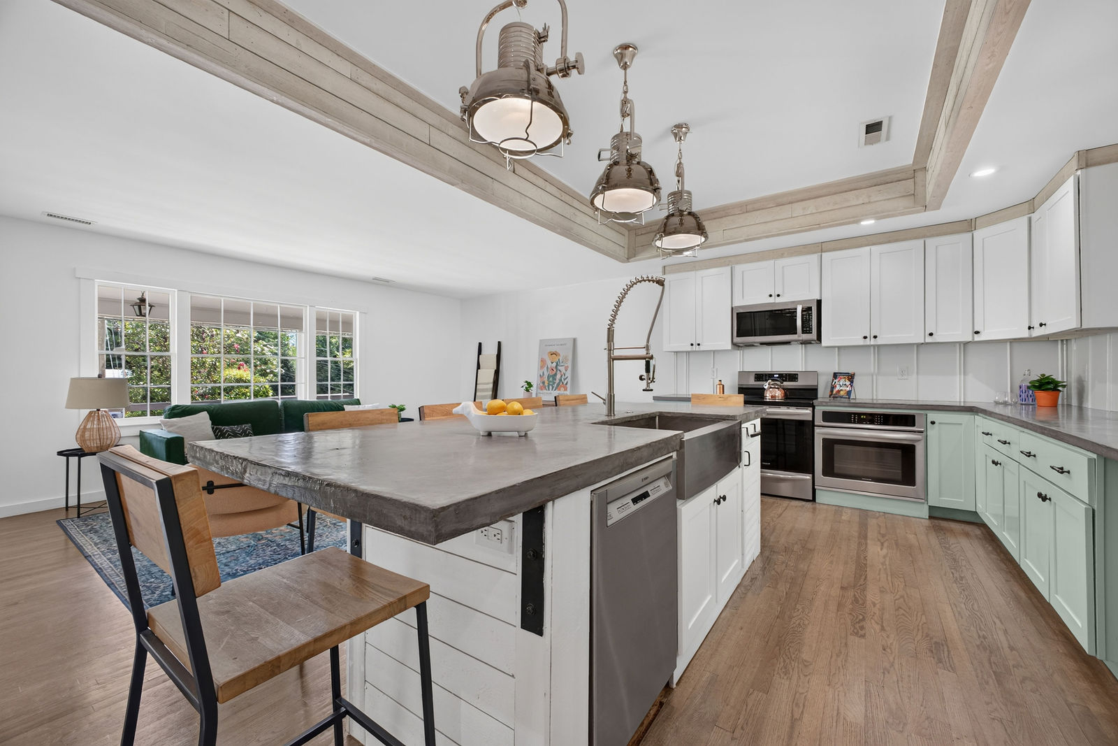 Open kitchen with concrete-topped island, sage green cabinetry, farmhouse sink and industrial pendant lighting