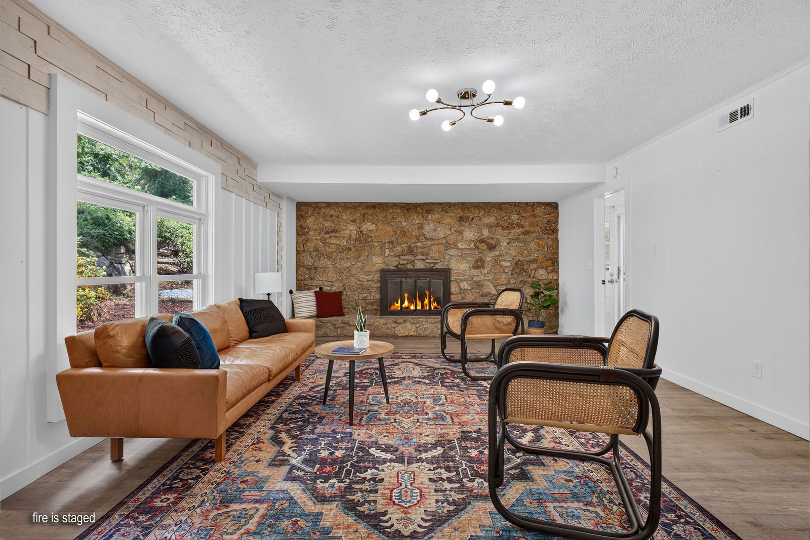 Lower-level living room with floor-to-ceiling stone wood-burning fireplace, leather sofa and large window to the woods