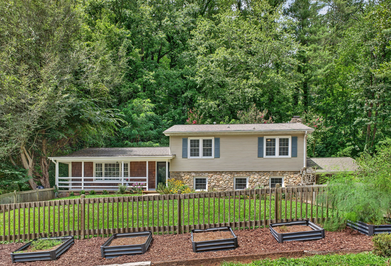 Rear view of the home set against a wooded hillside, with raised garden beds in the foreground