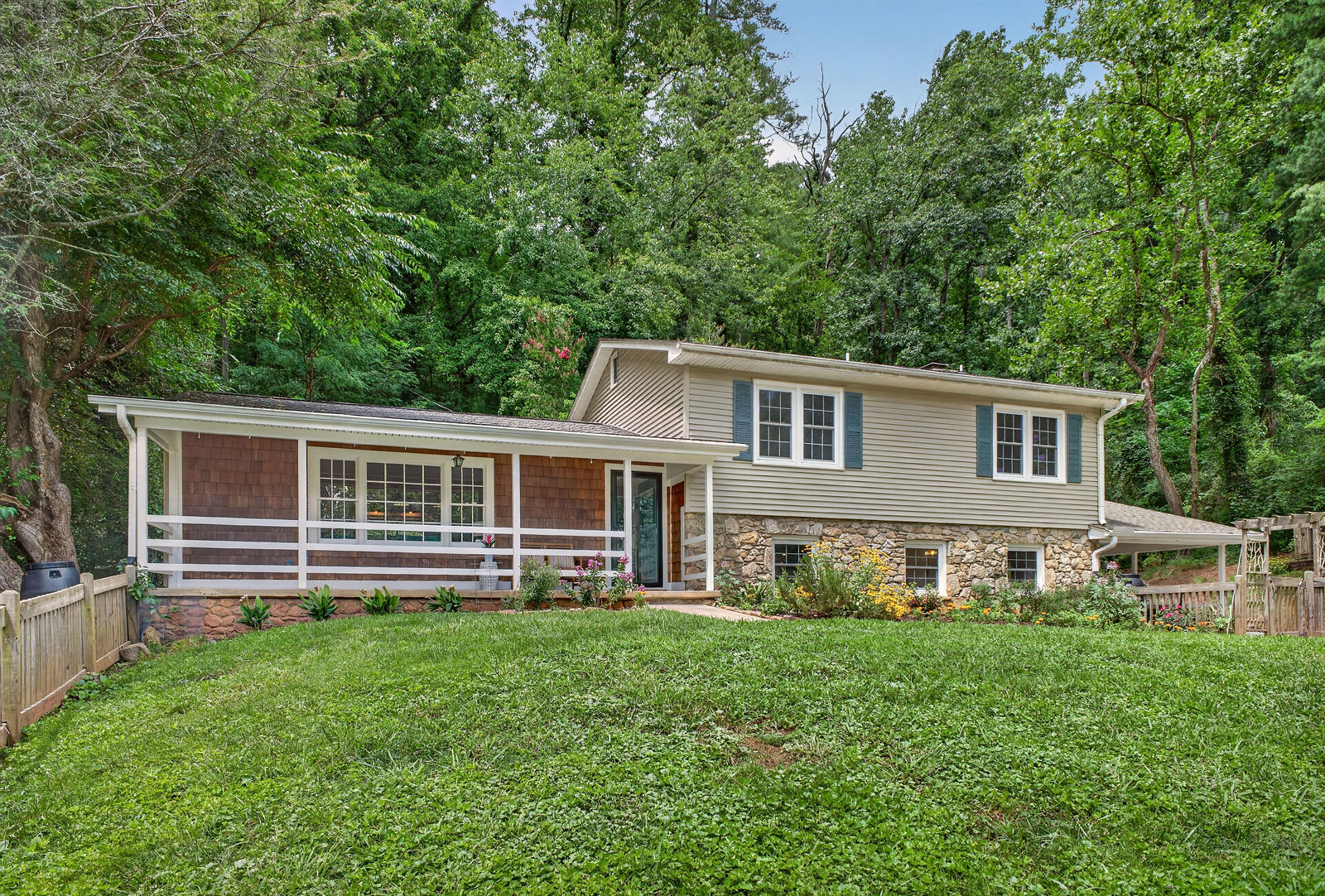 Front elevation of 23 Clearbrook Road, a tri-level home with stone foundation and covered porch, framed by mature woods