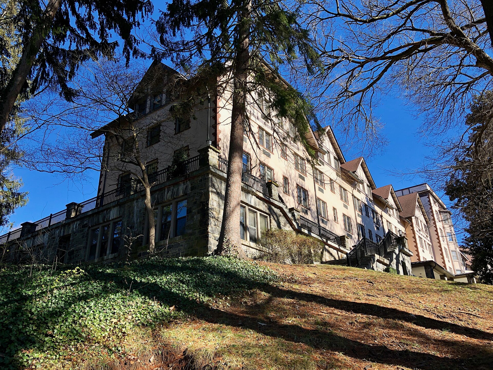 The Kenilworth Inn today, a large Tudor Revival building on a stone base seen from the hillside below